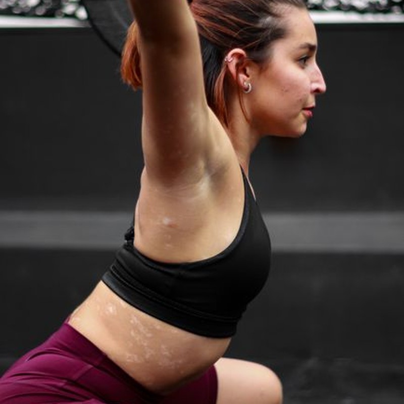Side profile of a woman lifting a barbell in a gym, showcasing strength and focus.