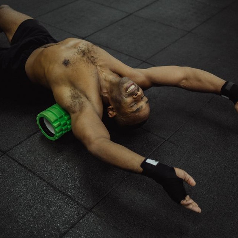 Shirtless man exercising with a foam roller in a fitness center.