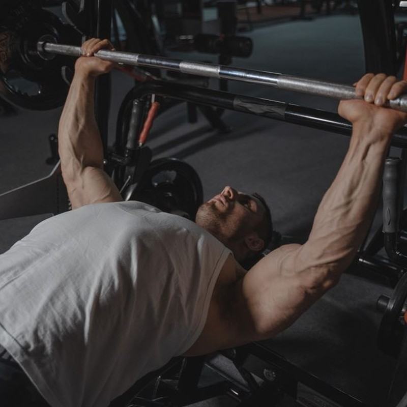 A focused man lifts heavy weights on a bench press machine in a dimly lit gym.