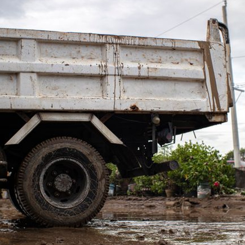 Aged vehicle with corrosion parked on roadway with mud against shrubs in town in daytime
