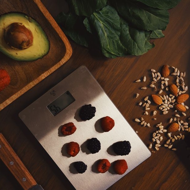 Top view of composed raw almond with seeds and avocado on table with berries on scales for cooking healthy dish