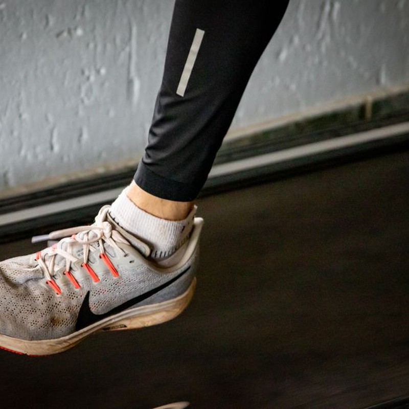 A detailed view of a sneaker mid-stride on a treadmill, showcasing active lifestyle footwear.