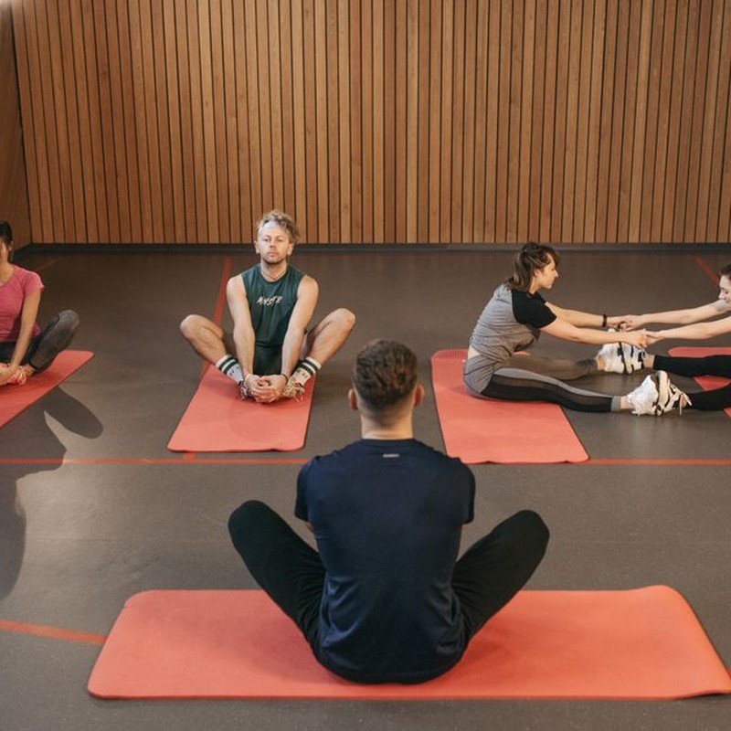 People engaging in a yoga class with red mats in an indoor wooden studio.