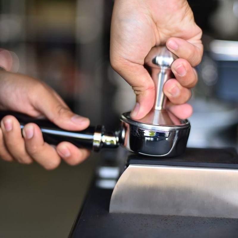 Close-up of a barista's hands using a tamper to prepare espresso in a portafilter.