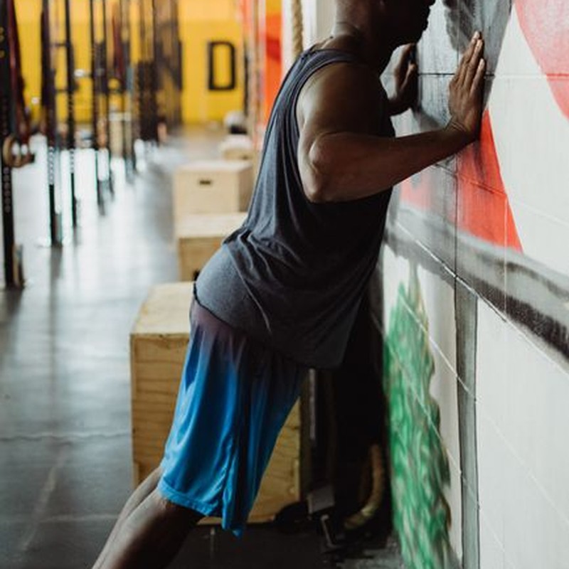 A man performs wall push-ups indoors, exhibiting strength and focus in a gym environment.