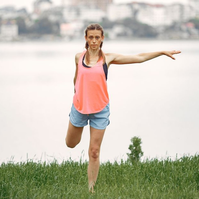 Woman exercising and stretching by a lakeside in a peaceful outdoor setting.