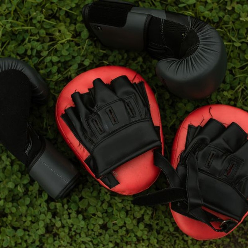 Close-up of boxing gloves and pads placed on green grass, emphasizing fitness and sports.