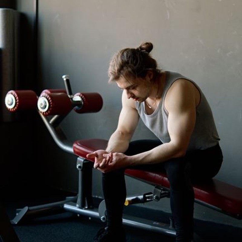 Caucasian man sitting on gym bench, looking tired after workout. Indoor fitness setting.