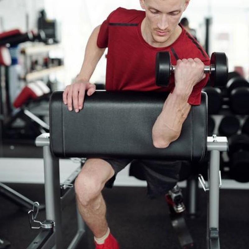 A determined man with a prosthetic leg lifting dumbbells in a gym, focused on fitness and strength.