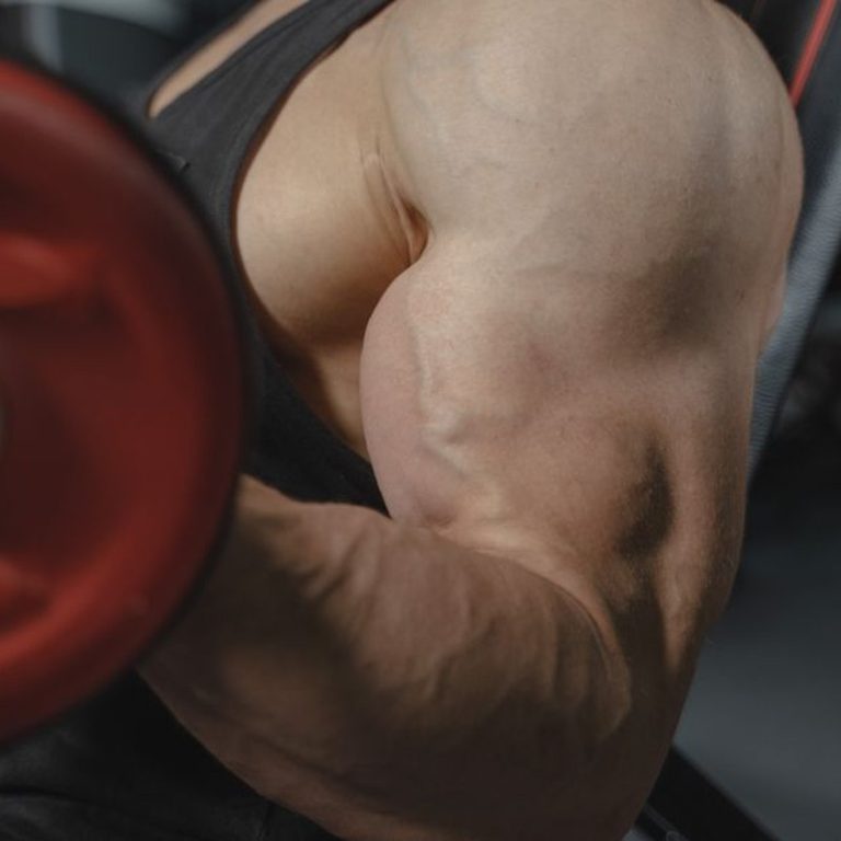 A focused view of a bodybuilder's arm muscles lifting a dumbbell in a gym setting.