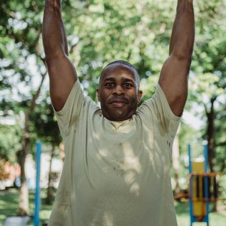 Adult man exercises on pull-up bar in a sunny outdoor park setting.