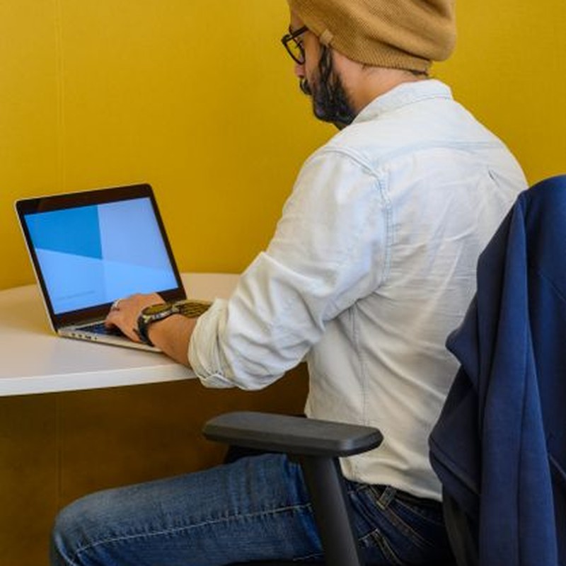 Bearded man in casual attire working on a laptop in modern office setting.