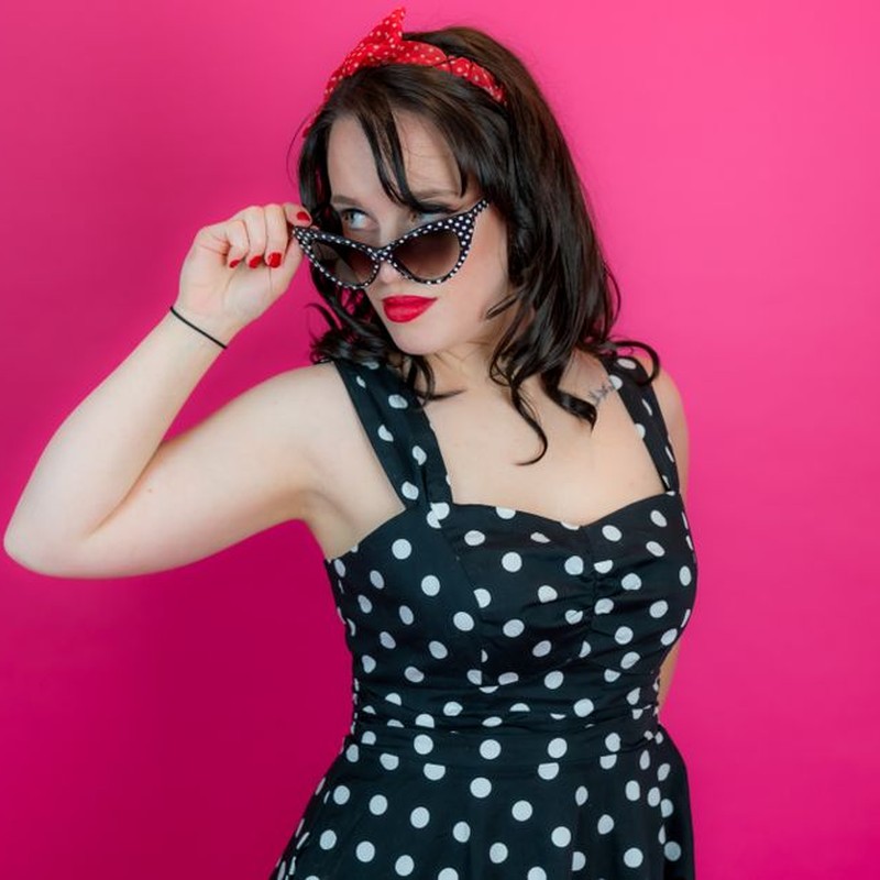 Stylish woman in polka dot dress and sunglasses embodying classic pin-up style with bold red lips.