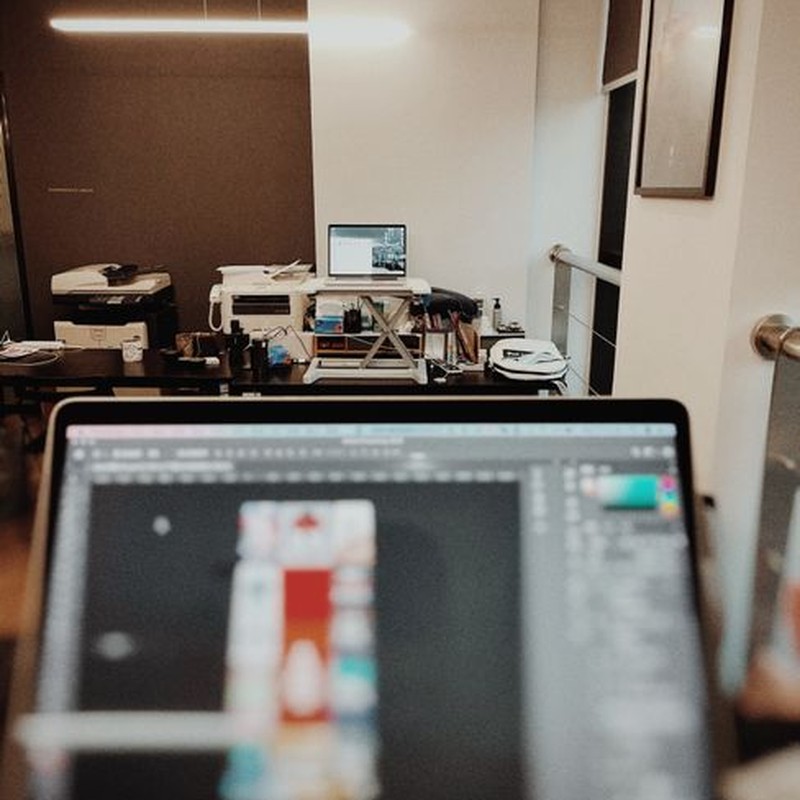 A contemporary office showing a laptop running design software in focus with desks and equipment in the background.