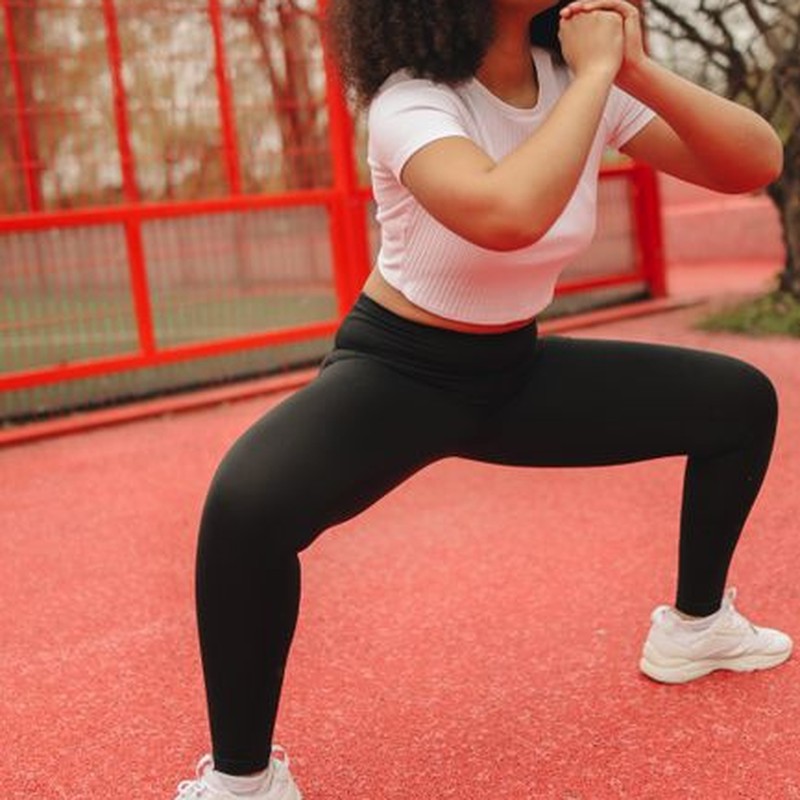 African American woman in sportswear squatting outdoors on a red court.