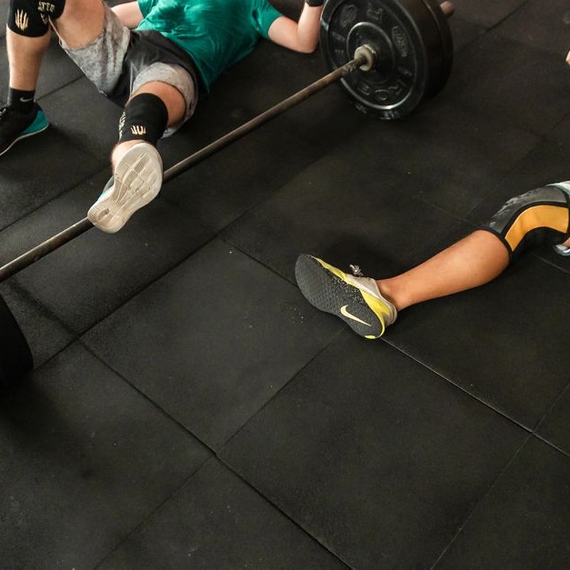 Athletes resting on a gym floor beside heavy barbells after an intense weightlifting session.
