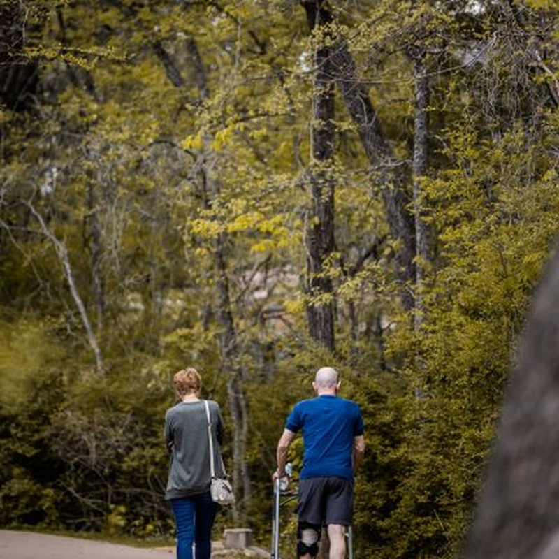 Back view of unrecognizable male leaning on walkers while walking in orthosis on broken leg with woman