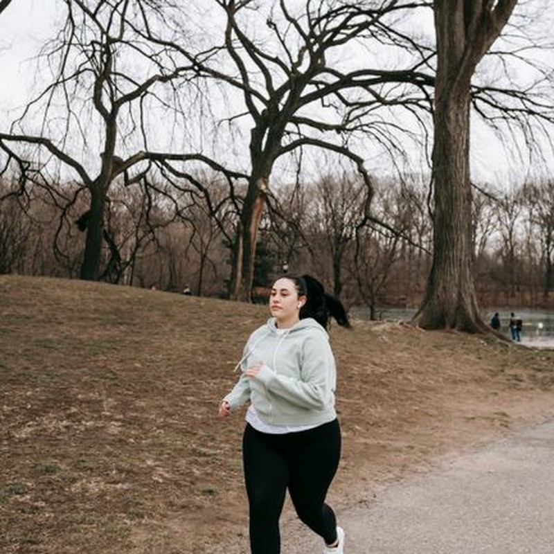 Full body motivated plus sized female in gray hoodie running in autumn park