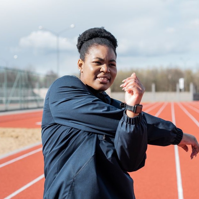 A woman stretches outdoors on a running track, promoting active and healthy living.
