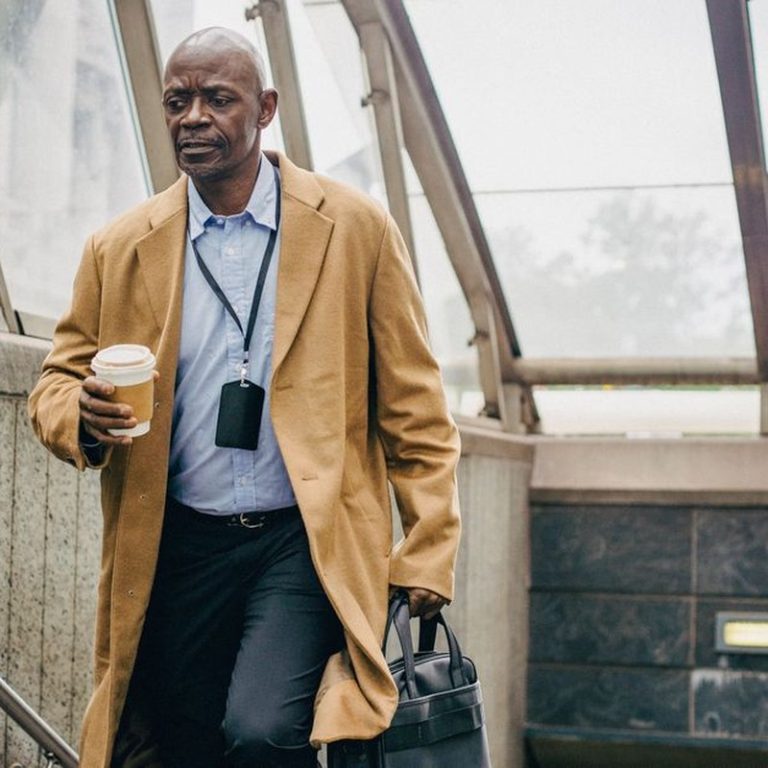 Pensive middle aged ethnic male office worker with takeaway coffee walking on staircase while looking down in building