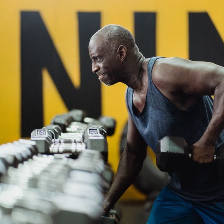 Strong senior man focusing on strength training with dumbbells in a vibrant gym.