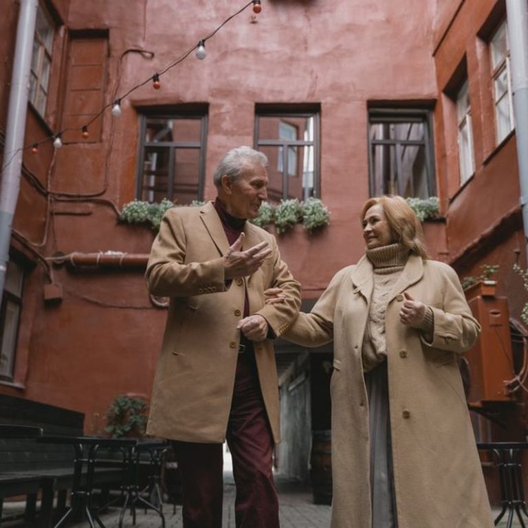 A joyous elderly couple walking hand in hand, sharing a moment in an urban setting.