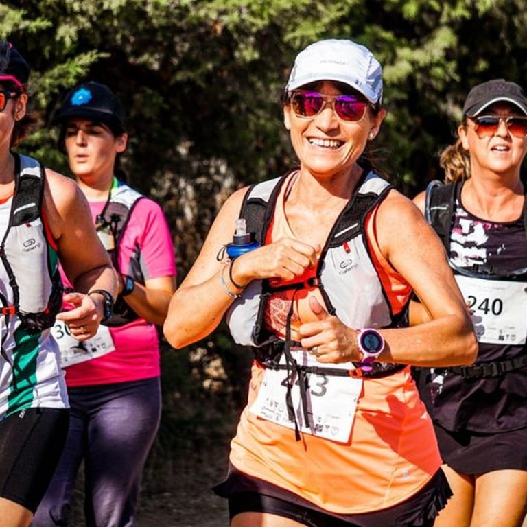 A group of smiling women participating in an outdoor marathon run with race numbers.