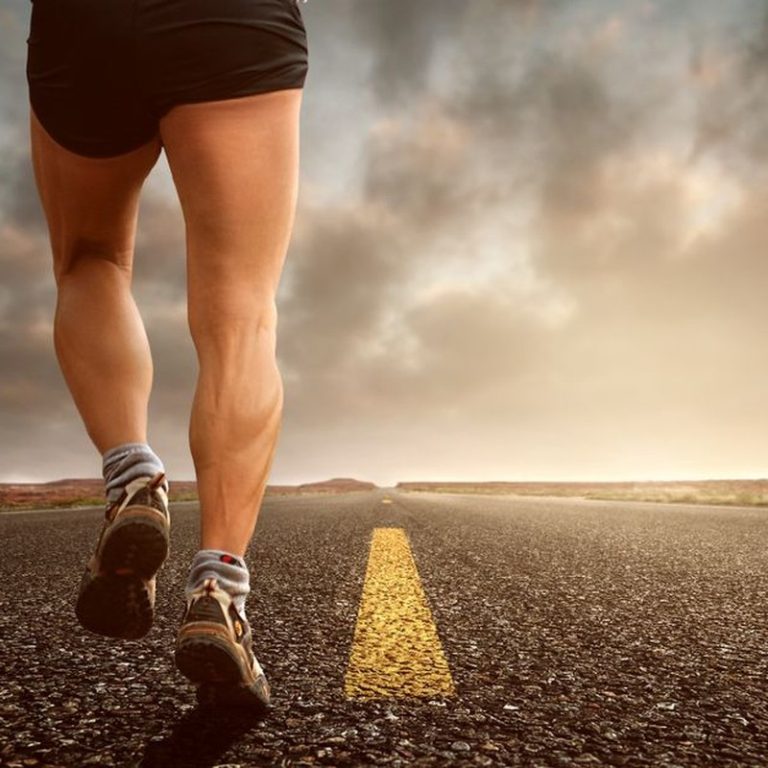 Runner's legs on a road during a sunset, symbolizing endurance and outdoor fitness training.