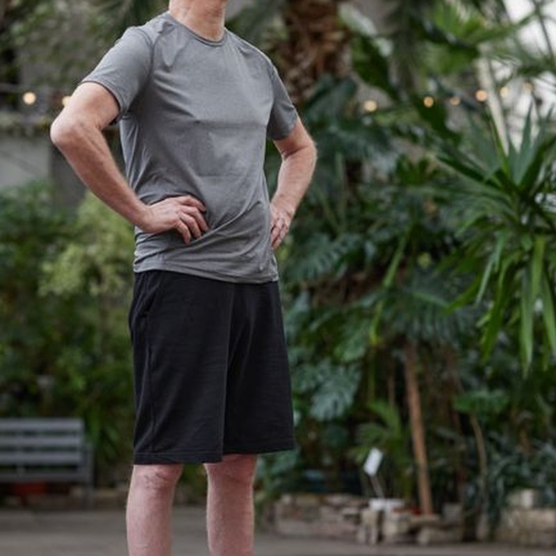 Smiling senior man performing yoga in an indoor greenhouse setting, promoting wellness.