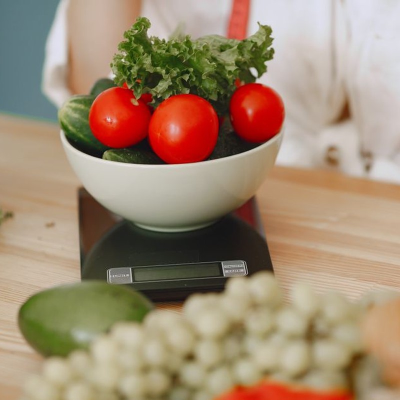 Colorful fresh vegetables including tomatoes and cucumbers on a kitchen scale for healthy eating.