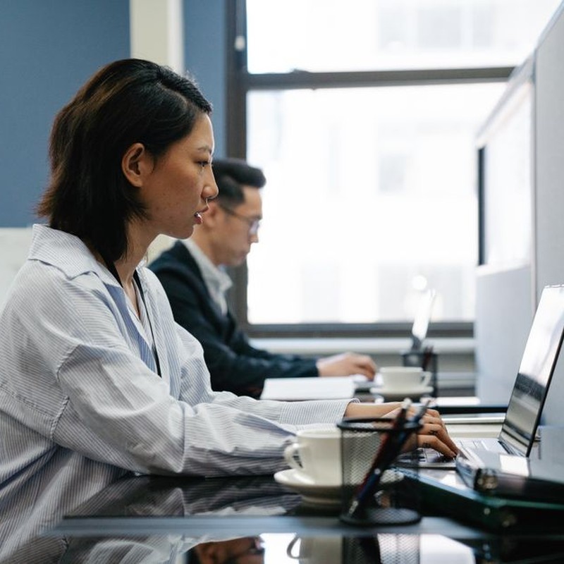Two professionals working diligently on laptops in a modern office setup, capturing productivity and teamwork.