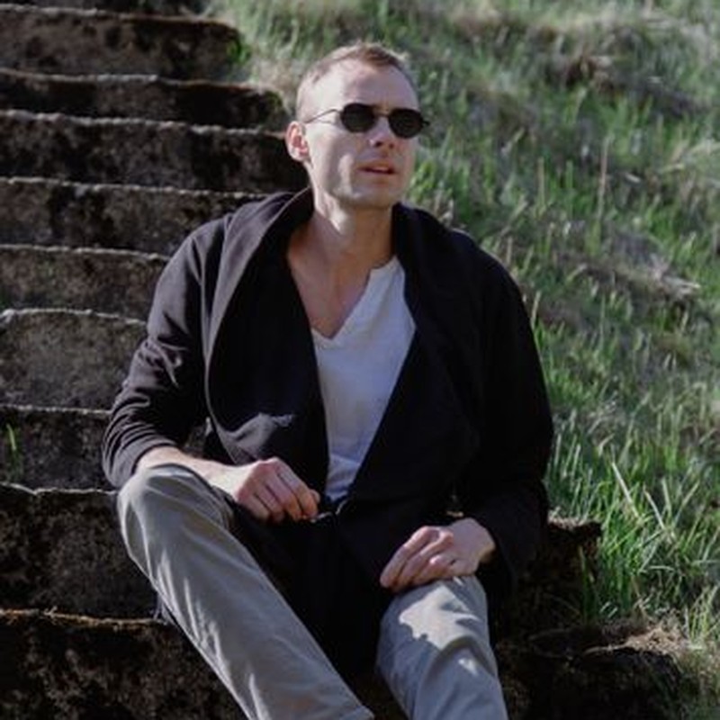 A man sits casually on outdoor stone steps, enjoying a sunny day.