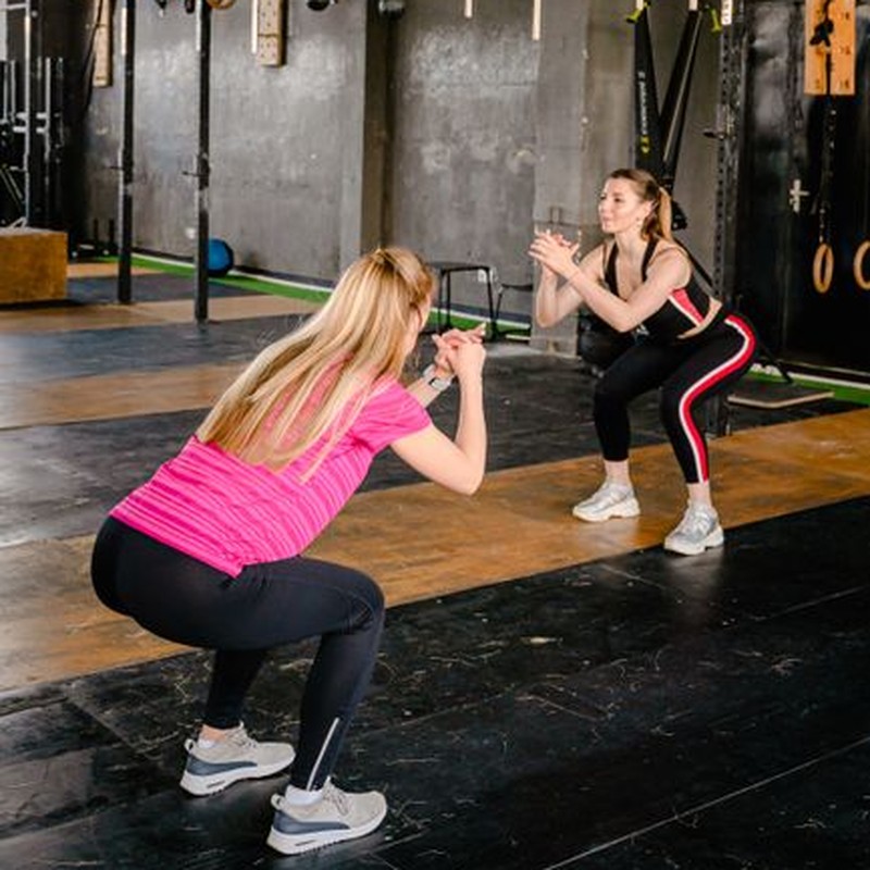 Two women performing squats in a modern gym setting, enhancing fitness and motivation.