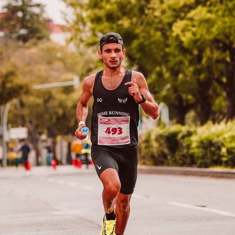 Focused male athlete running in a marathon, wearing a tank top and holding a bottle of water.