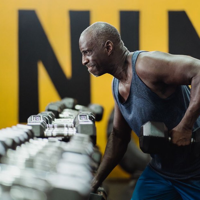 Strong senior man focusing on strength training with dumbbells in a vibrant gym.