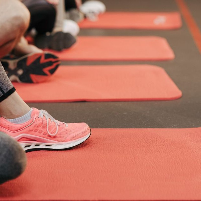 Participants in exercise class wearing colorful sneakers and sitting on red mats.