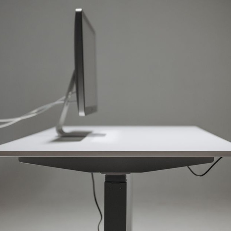 Side profile of a modern office desk with a computer monitor, emphasizing minimalism and technology.