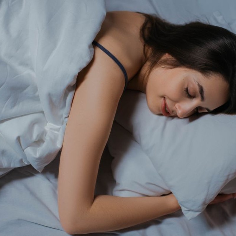 Serene young woman sleeping in cozy bed with white linens. Peaceful and relaxed.
