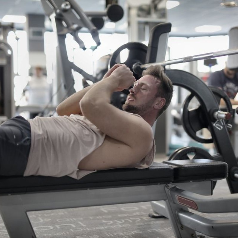 Focused muscular sportsman in modern sportswear preparing to workout with heavy barbell on bench training in modern gym