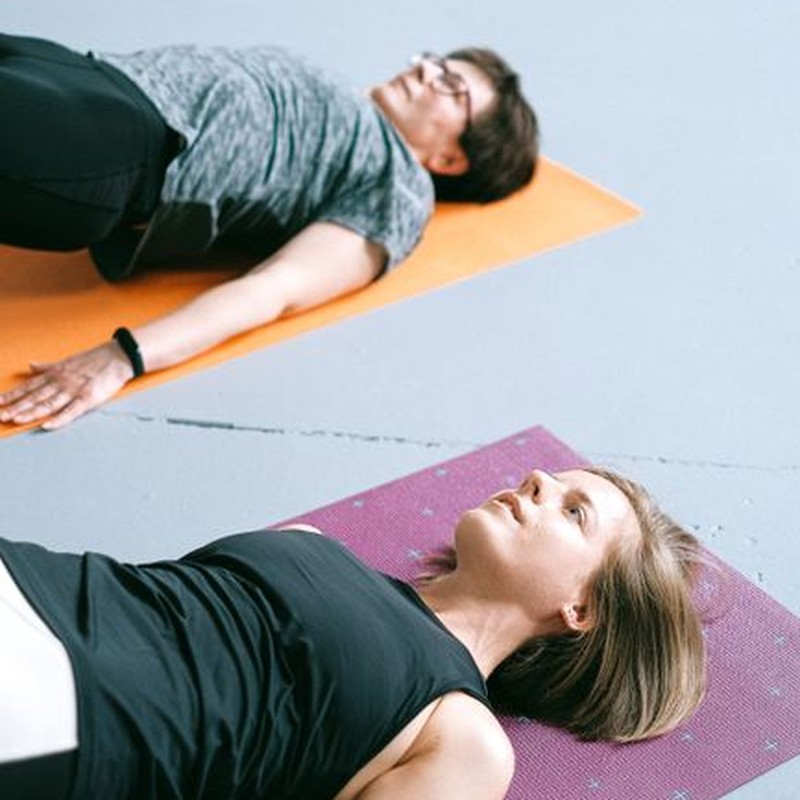 Two women practicing yoga poses on colorful mats in a studio setting, promoting a healthy lifestyle.