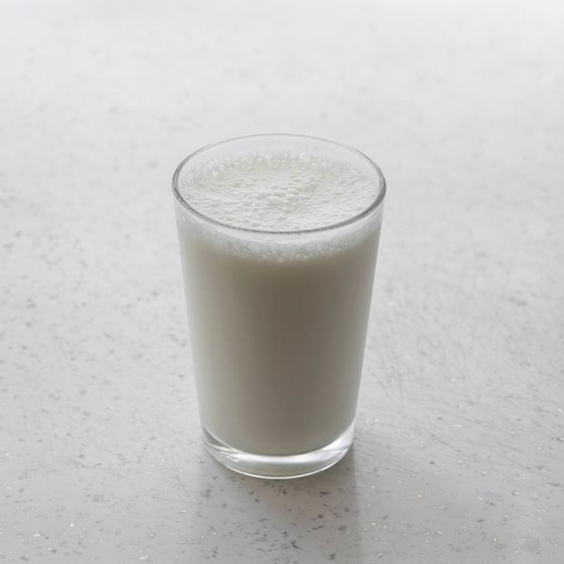 A frothy glass of milk on a textured white surface, captured with minimalism.