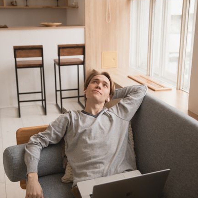 A young man relaxes with a laptop on the sofa in a modern living room.