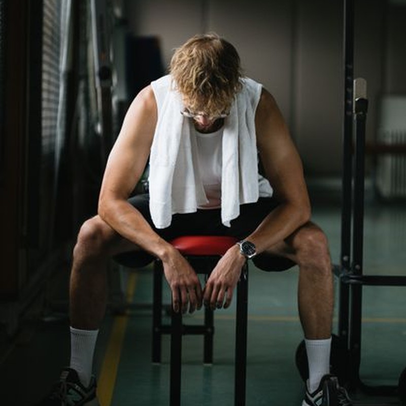 Full body of muscular male in sportswear sitting on bench and resting after training