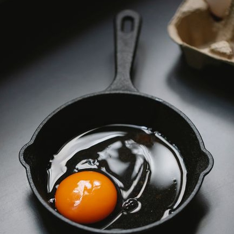 From above of frying pan with uncooked egg near cardboard container in kitchen
