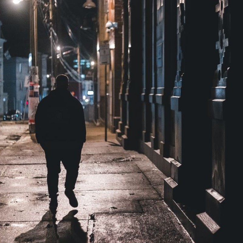 Anonymous silhouette male walking on wet sidewalk on old city street in dark night