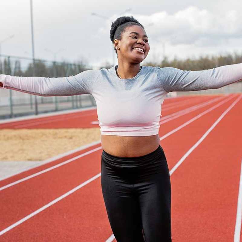 A cheerful young woman enjoying her workout on an outdoor running track, embracing fitness and wellness.