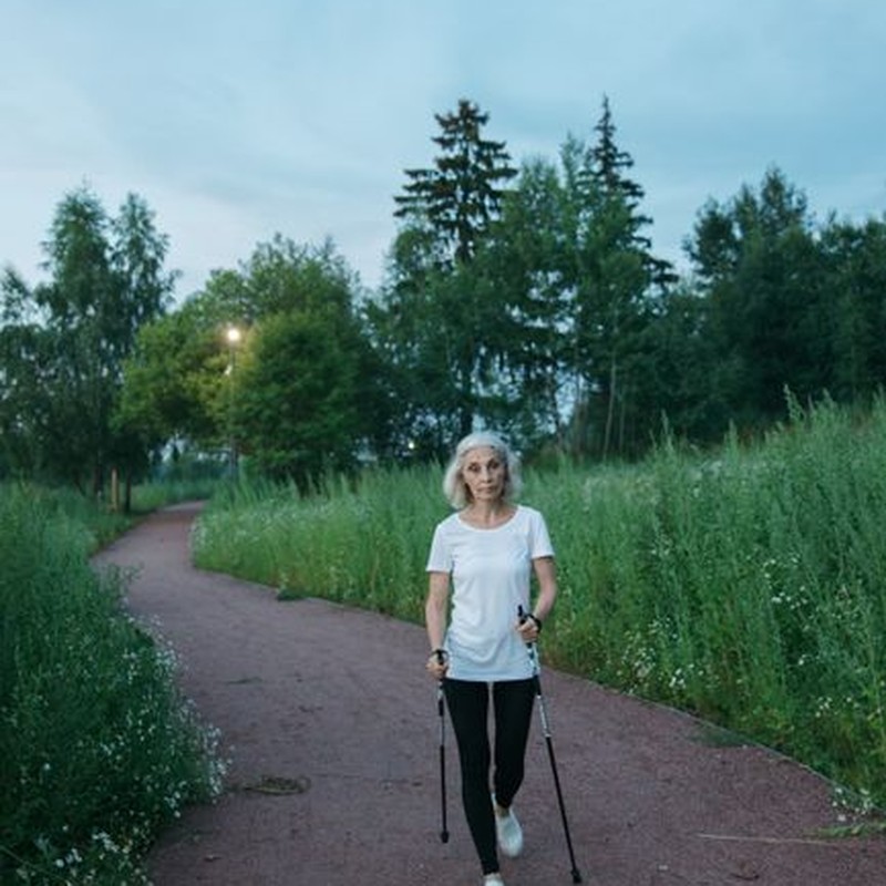 Senior woman enjoying a Nordic walk in lush green park setting.