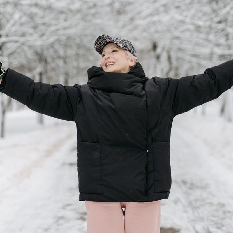Senior woman smiling and raising arms while enjoying a winter walk with ski poles outdoors.