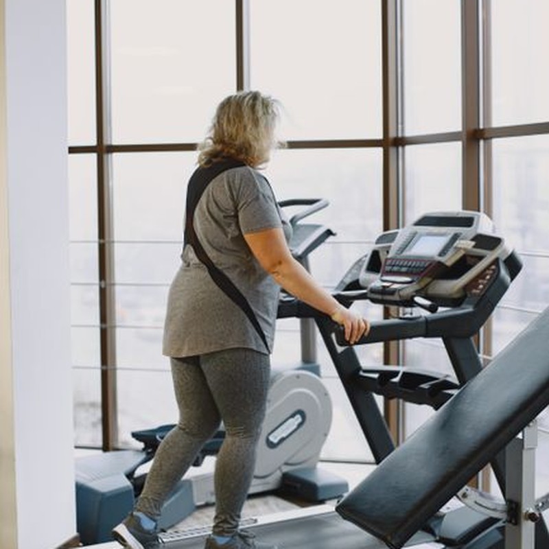 Mature woman walking on a treadmill in a modern gym with large windows