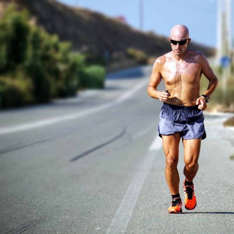 A determined jogger runs on a sunlit road in Crete, Greece. Perfect for fitness and travel themes.